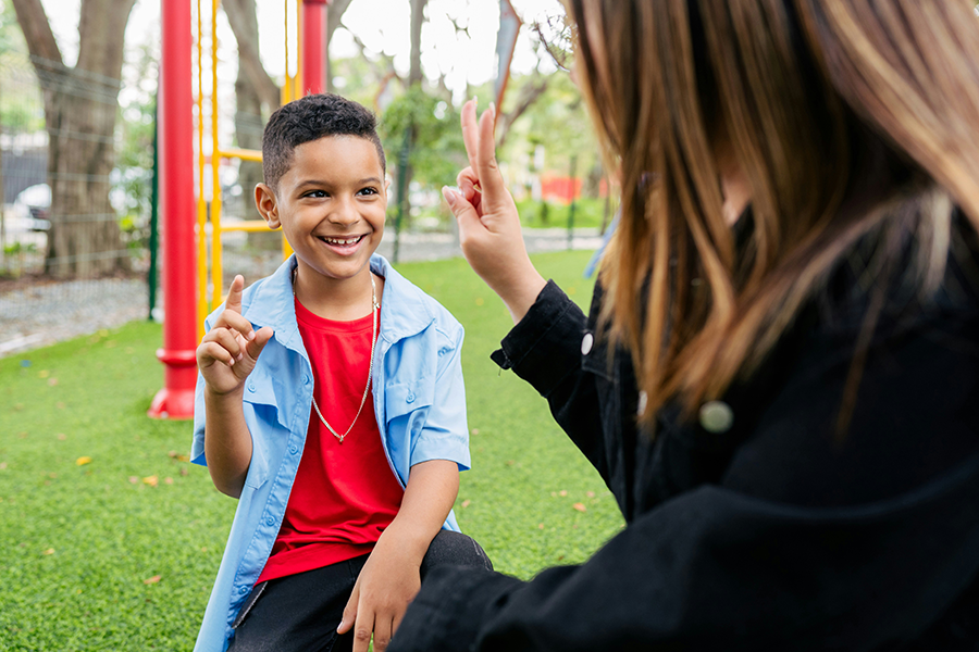 Boy and woman signing to each other at a park