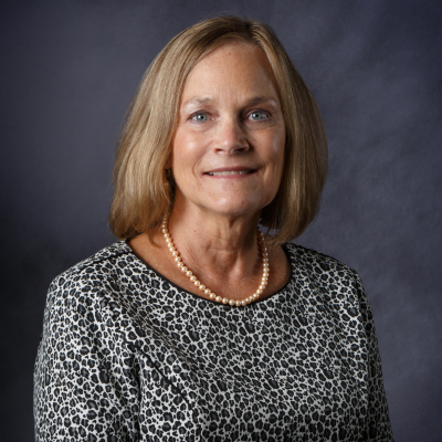 Professional photo of a person with a nice blouse and necklace on. She is smiling at the camera and her body is turned towards her left.