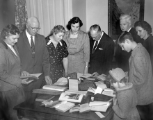 Black and white historical photo of a group of people looking at books on a table during the National Library Week, 1958