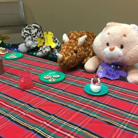 A leopard, a rhino, and a teddy bear sitting at a table with plates and cookies/cupcakes